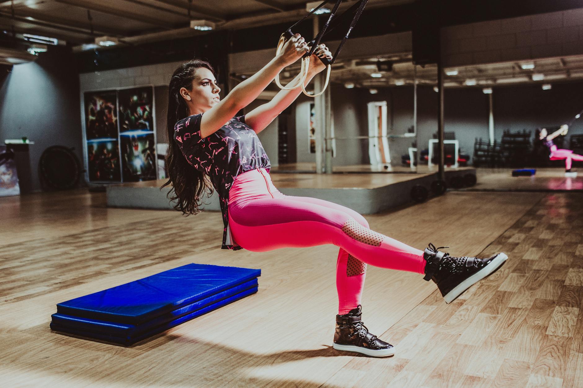 determined sportswoman squatting with suspension straps in modern gym