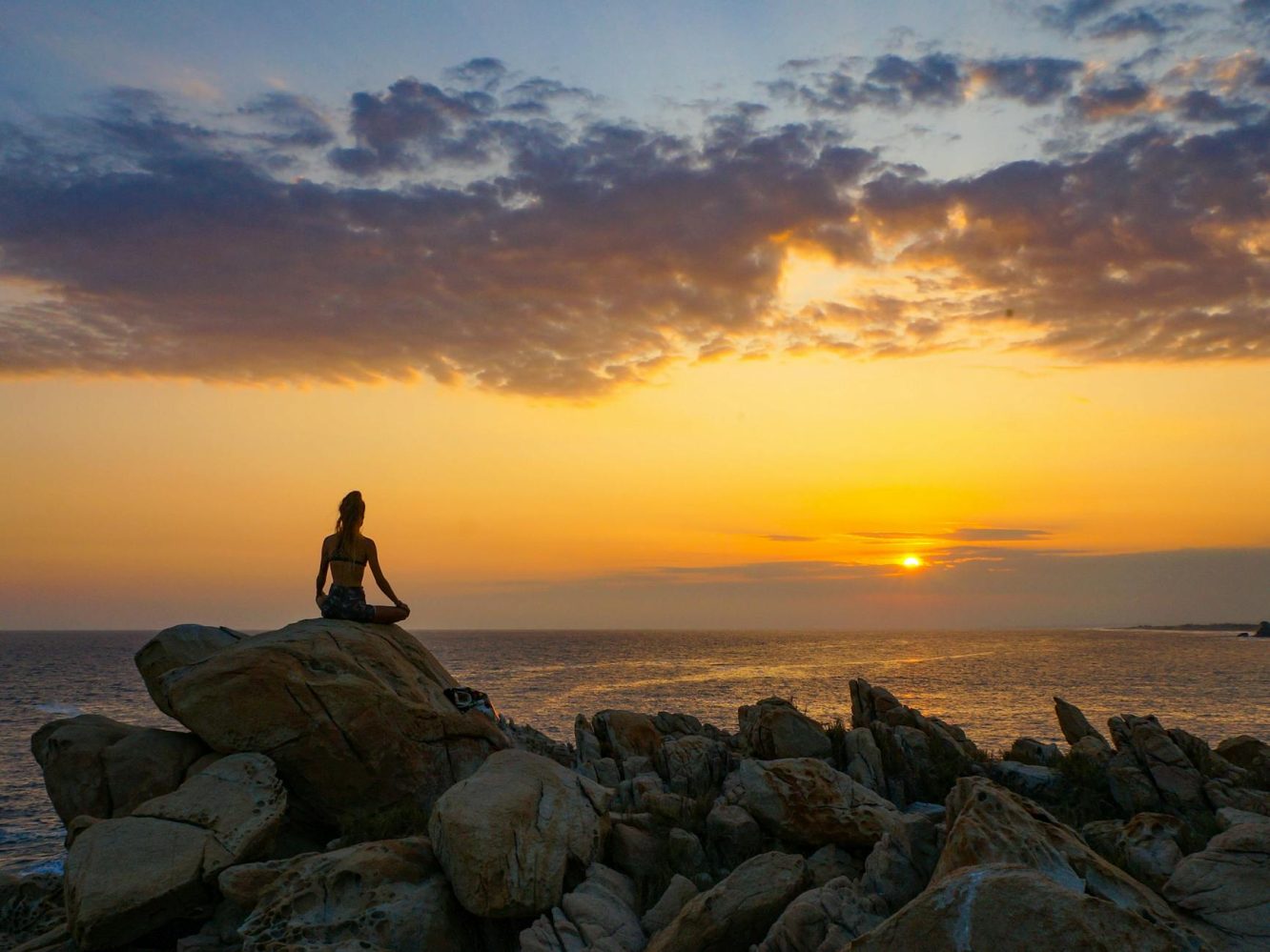 woman meditating on top of a boulder in front of sea